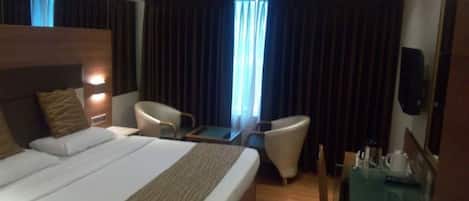 A hotel room with a large bed, two armchairs, a small table, and a TV.