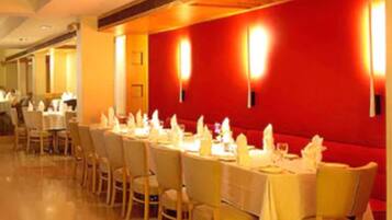 A restaurant with a long table set for a meal, red walls, and wall-mounted lights.