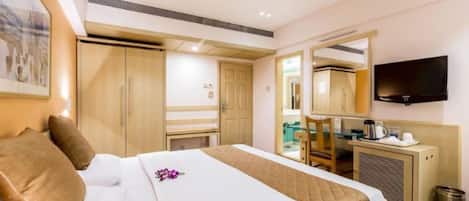 A hotel room with a bed, a desk, a chair, a television, and a mirror.