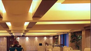 A spacious banquet hall with rows of white chairs and tables, a stage with floral decorations, and a polished floor. - The Royal Orchid (Mumbai)