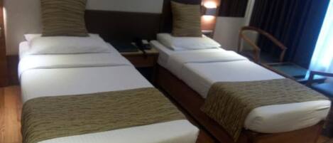 Ein Hotelzimmer mit zwei Einzelbetten, Holz-Kopfteilen und einem Nachttisch mit Lampe.