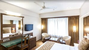 A hotel room with a bed, a desk, a chair, a television, and a window with curtains. - The Royal Orchid (Mumbai)