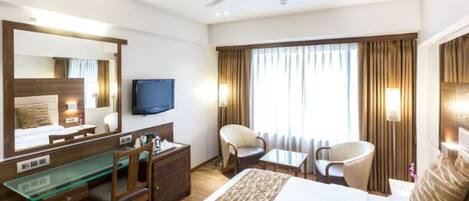 A hotel room with a bed, a desk, a chair, a television, and a window with curtains.