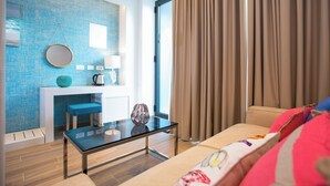 A modern living room with a glass coffee table, a sofa with colorful cushions, a blue textured wall, and a large window with curtains. - Villa Diamond (Zupa dubrovacka)