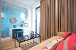 A modern living room with a glass coffee table, a sofa with colorful cushions, a blue textured wall, and a large window with curtains. - Villa Diamond (Zupa dubrovacka)