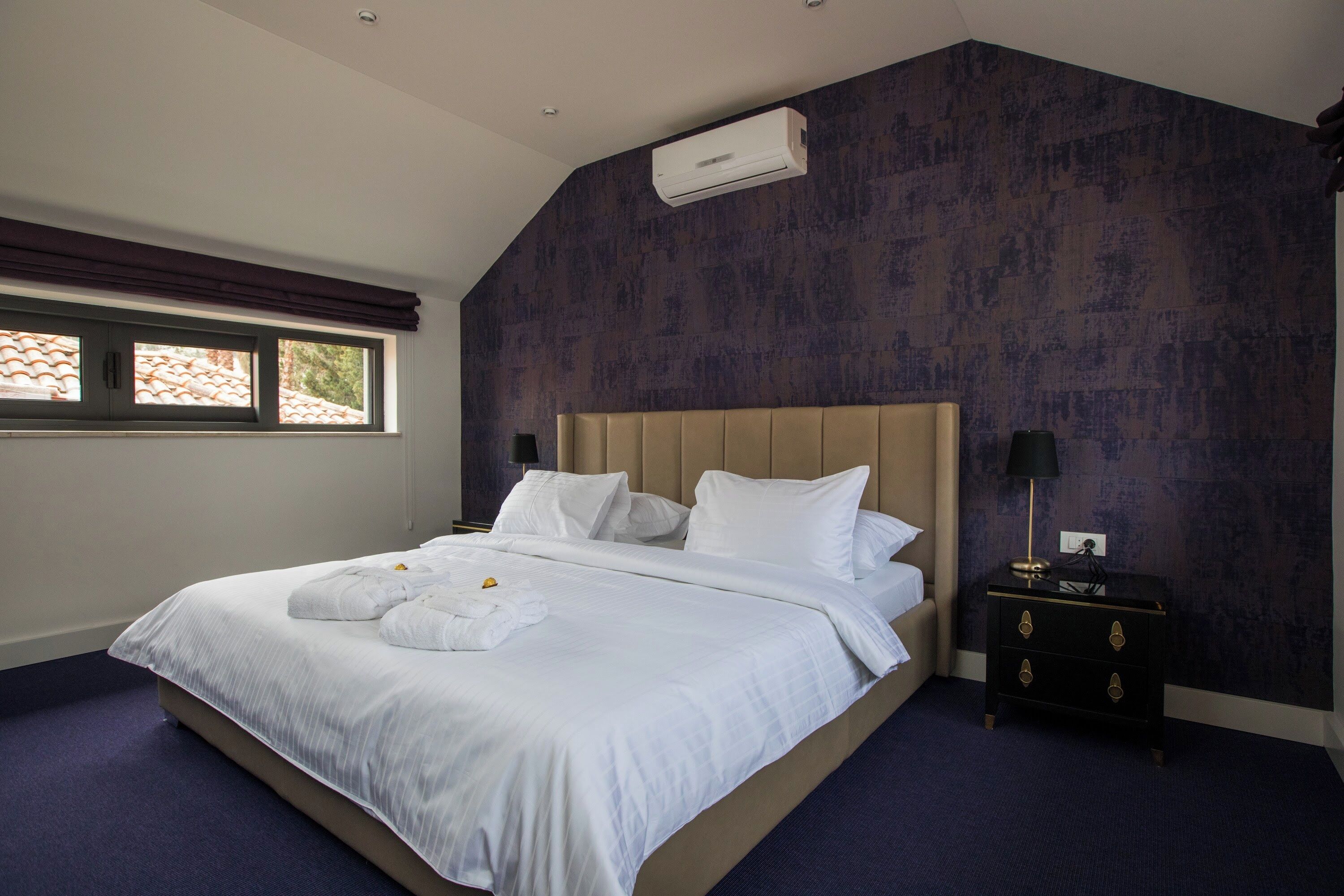 Ein Hotelzimmer mit einem großen Bett, einem Nachttisch, einer Lampe und einem Fenster mit Vorhängen.