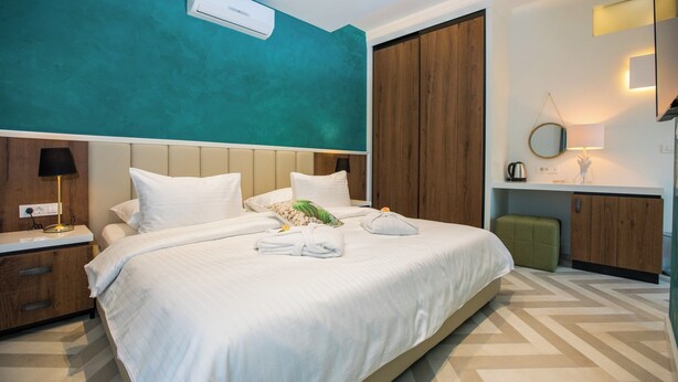 A hotel room with a large bed, a wooden wardrobe, a small green stool, and a bedside table with a lamp. - Villa Diamond (Zupa dubrovacka)