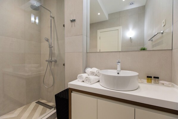 Une salle de bain moderne avec une douche à l’italienne, un grand miroir, un lavabo rond et des serviettes soigneusement pliées.
