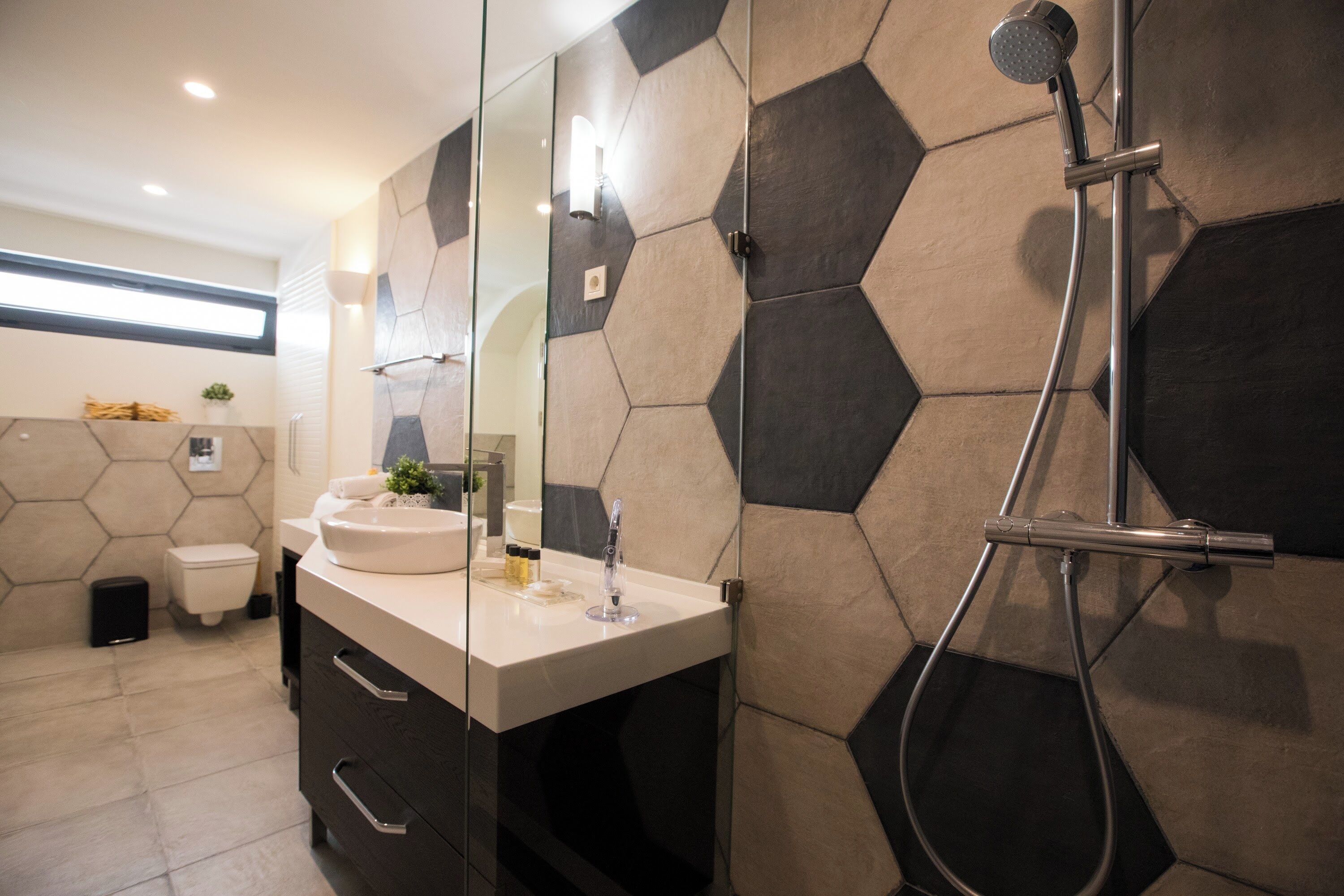 A modern bathroom with a hexagonal tile wall, a large mirror, a sink, and a shower.