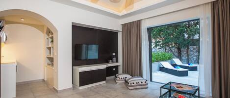 Una sala moderna con televisor de pantalla plana, una mesa de centro de vidrio y una zona de estar con cojines.