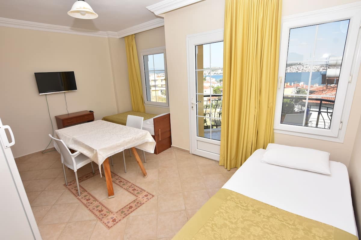 Une chambre d’hôtel avec un lit, une table à manger avec des chaises, un téléviseur fixé au mur et un balcon avec des rideaux jaunes.