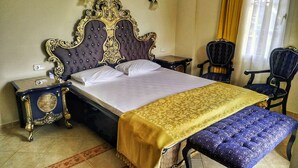 Un dormitorio con una cama grande, una mesita de noche, un banco, dos sillas y una ventana con cortinas.