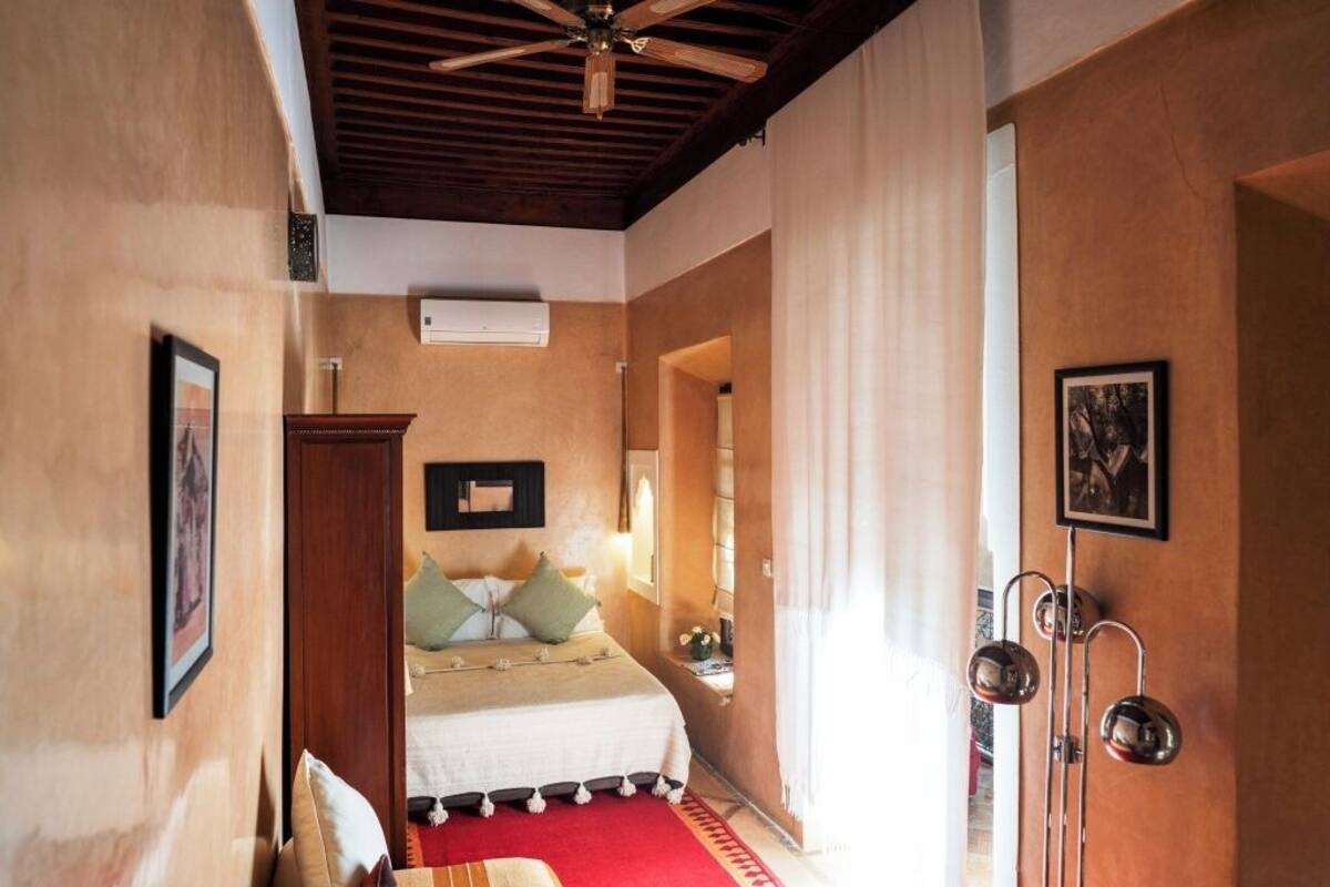 A bedroom with a bed, a wooden ceiling, a red rug, and a wall-mounted light fixture.