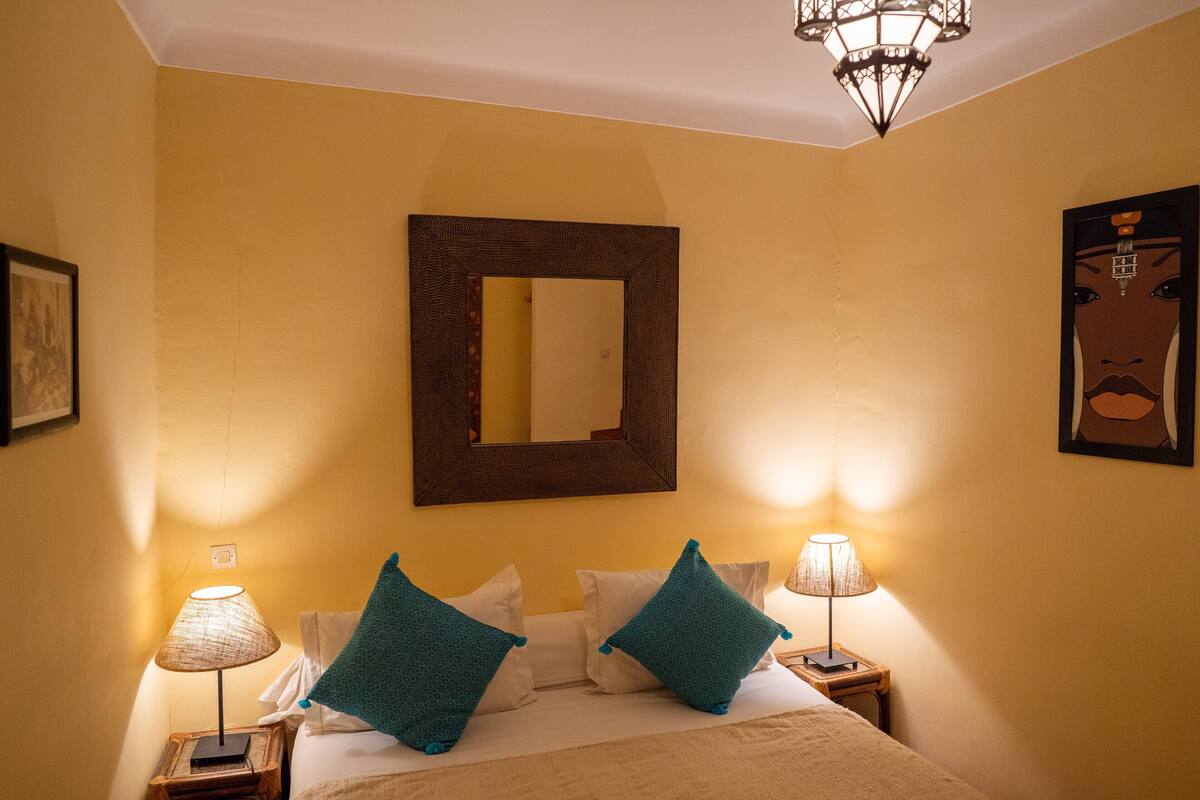 A hotel room with a bed, two bedside lamps, a large mirror, and a wall-mounted artwork.