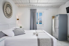 A bedroom with a bed, a wardrobe, a window with curtains, and a wall-mounted decorative item. - Kalergis Studios (Naxos)