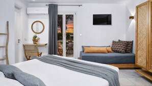 Ein modernes Schlafzimmer mit Bett, Sofa, Sessel, Fernseher und Blick ins Freie.