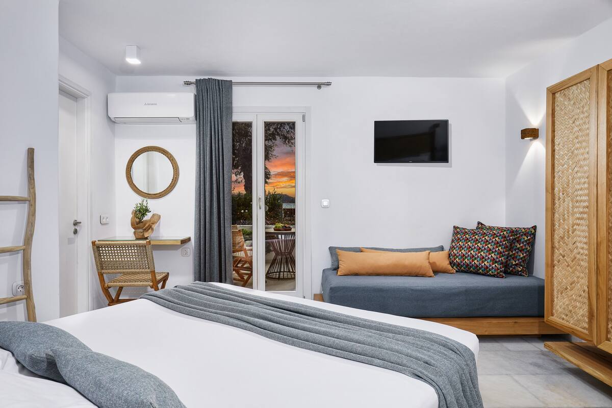 A modern bedroom with a bed, a sofa, a chair, a TV, and a view of the outdoors.