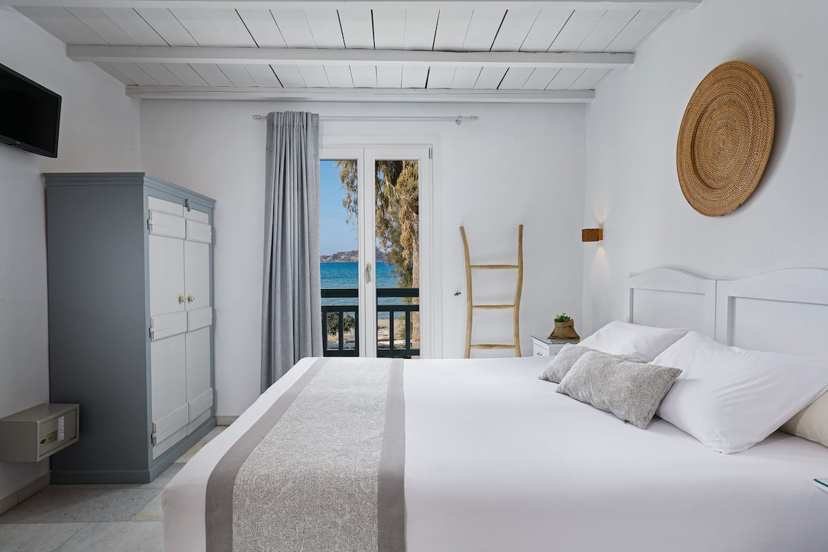 A bedroom with a bed, a wardrobe, a desk, and a view of the sea.