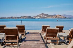 A beach with wooden lounge chairs and a wooden walkway leading to the water. - Kalergis Studios (Naxos)