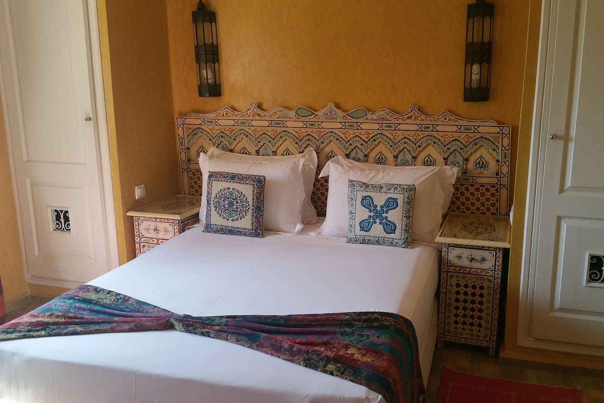 A bed with a colorful bedspread, two decorative pillows, and a patterned headboard.