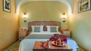 A traditional room with a large bed, ornate headboard, two nightstands with lamps, and a tray with food and drinks on the bed. - Villa Des 3 Golfs (Marrakech)