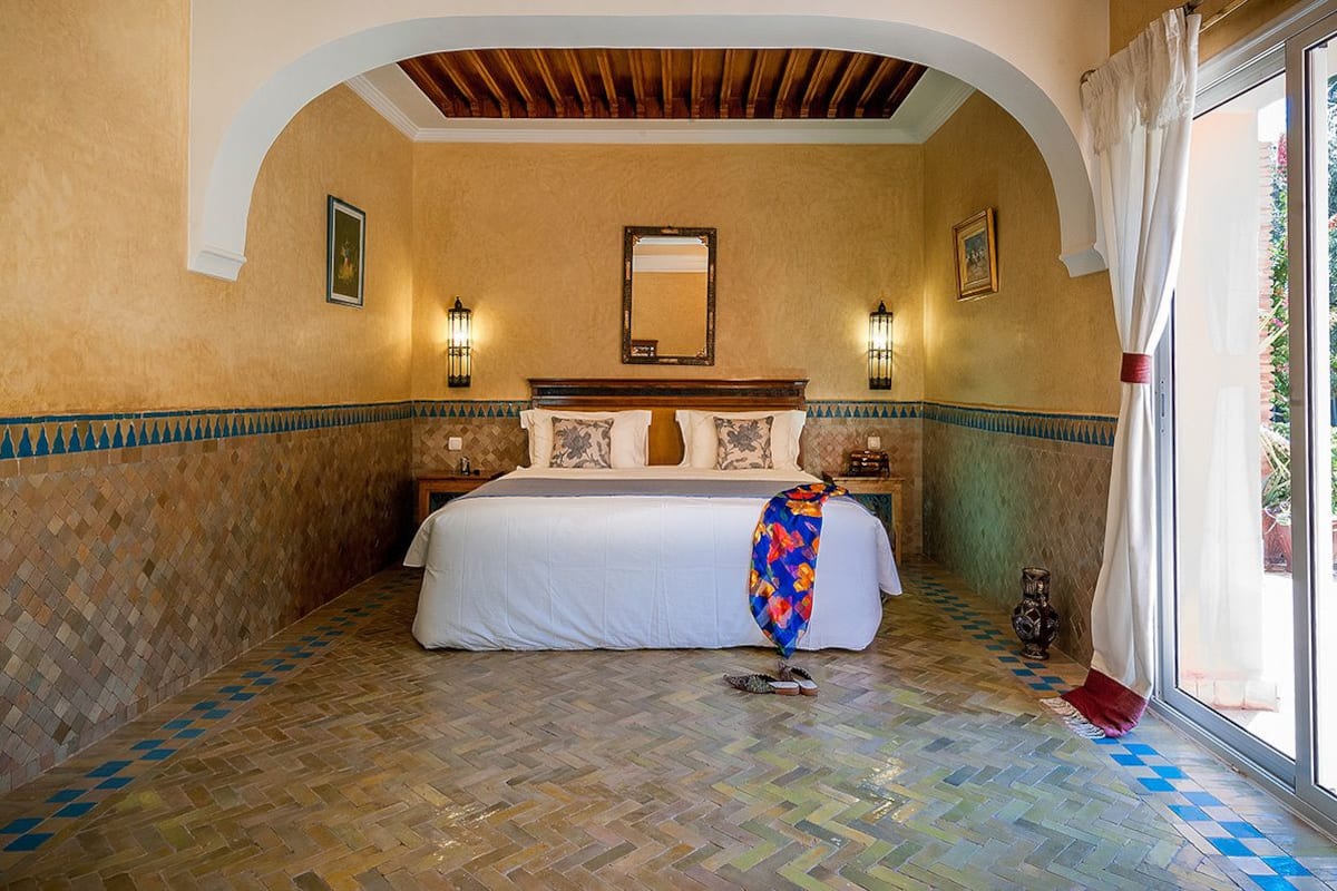 A bedroom with a large bed, a wooden ceiling, and a tiled floor.