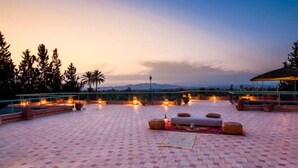 A rooftop terrace with a checkered floor, outdoor seating, and a view of the mountains at dusk. - Villa Des 3 Golfs (Marrakech)