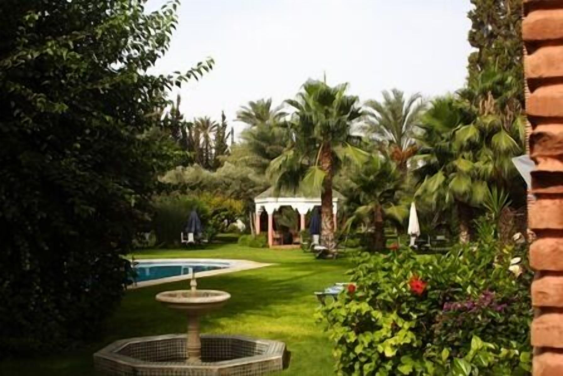 A garden with a fountain, palm trees, and a gazebo.