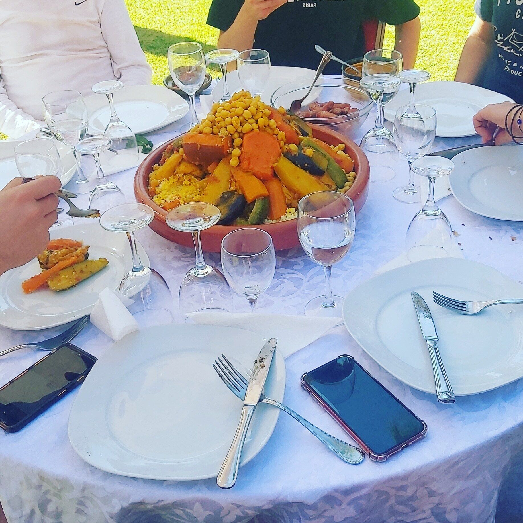 A dining table with a large central dish of mixed vegetables, surrounded by empty plates, glasses, and cutlery.