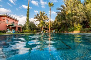 A swimming pool with clear blue water, surrounded by palm trees and a building with a balcony. - Villa Des 3 Golfs (Marrakech)