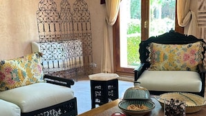 A traditional room with a sofa, a dining table with snacks, and a decorative metal fence. - Villa Des 3 Golfs (Marrakech)