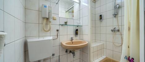 A bathroom with a toilet, sink, mirror, shower, and a glass shelf.