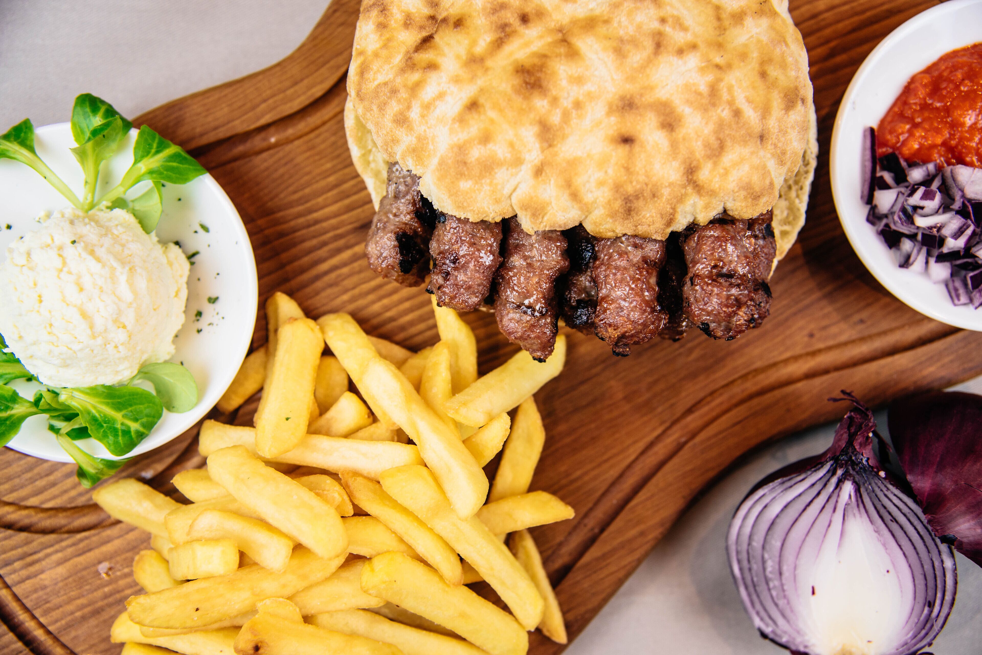 A meal consisting of a meat pie, French fries, a side salad, and a bowl of red onion relish.