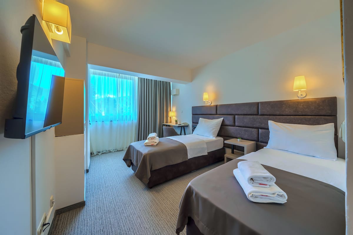 Habitación de hotel con dos camas, televisión, lámparas de noche, escritorio y ventana con cortinas.
