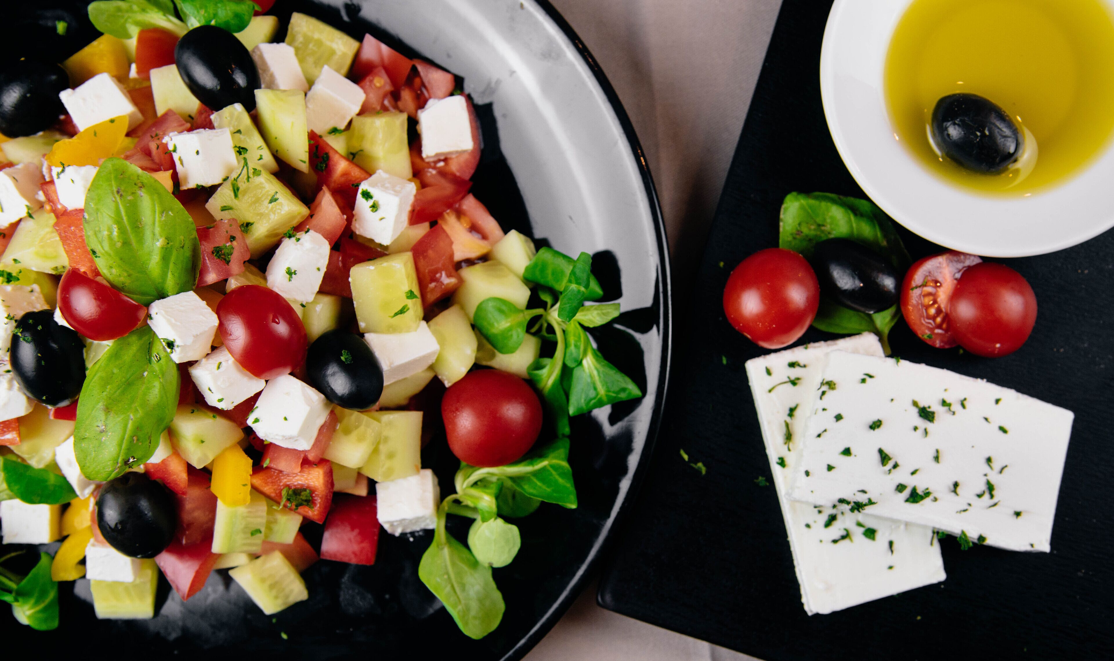 A salad with feta cheese, olives, tomatoes, and greens on a plate.