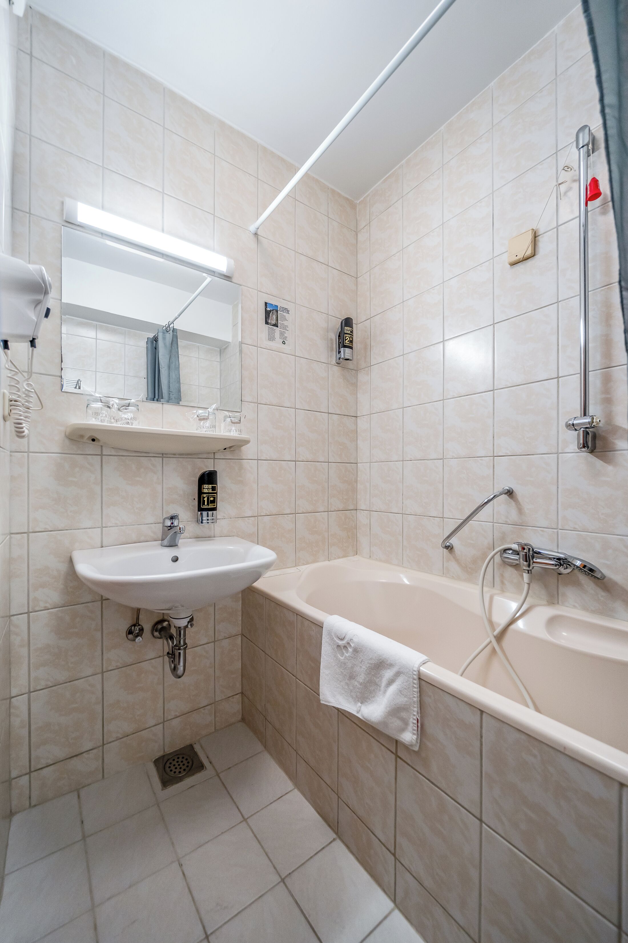 Een badkamer met een wastafel, spiegel, handdoekrek, douche en een lamp.