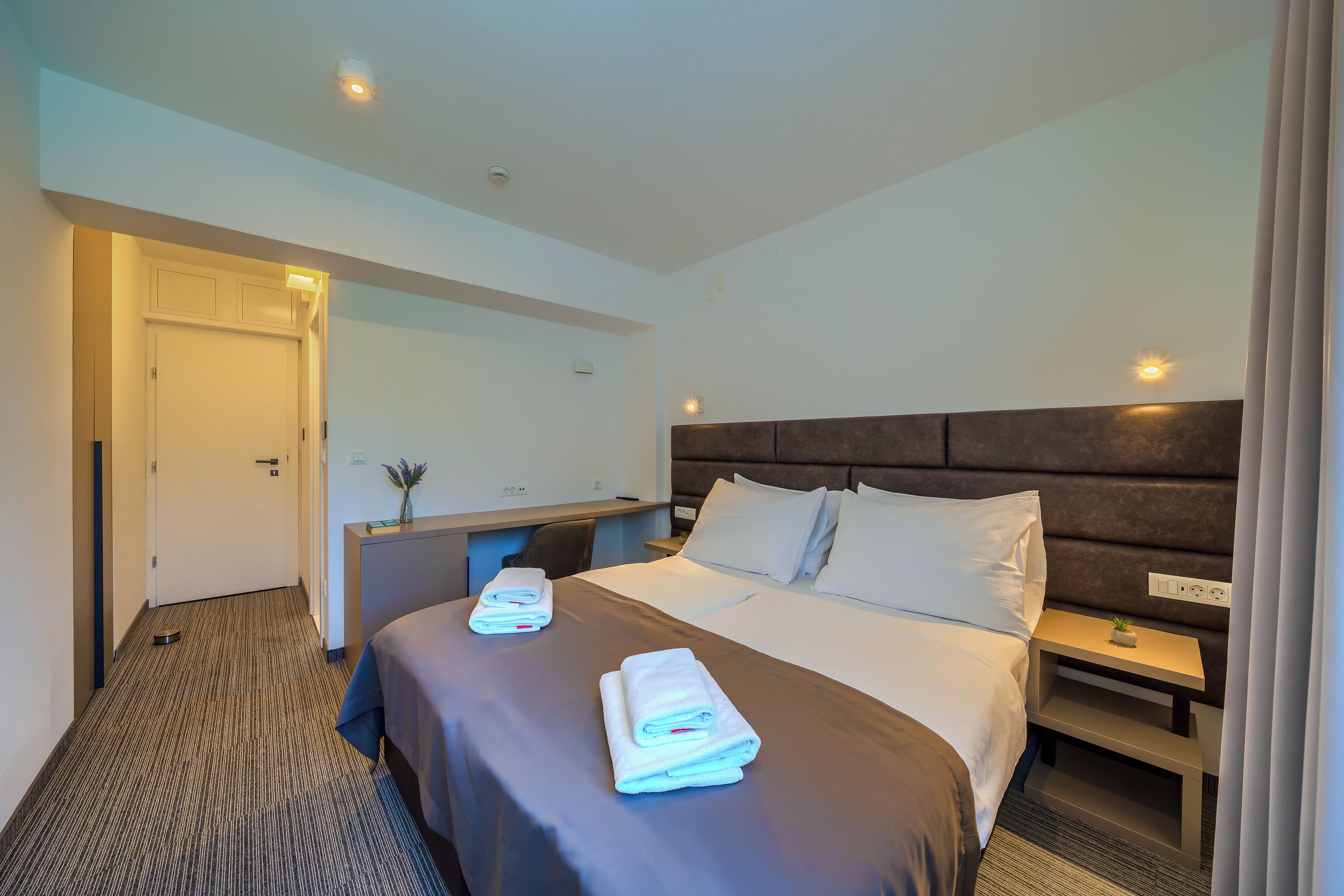 Una habitación de hotel con cama, mesita de noche, escritorio y espejo.