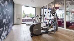A gym with treadmills and an elliptical machine, large windows, and a view of the outside.