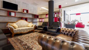 A modern lobby with a sofa, chairs, a large potted plant, and a flat-screen TV mounted on the wall.
