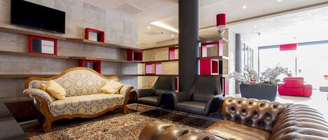 A modern lobby with a sofa, chairs, a large potted plant, and a flat-screen TV mounted on the wall.