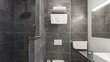 Un baño moderno con zócalos de mármol oscuro, ducha, inodoro y lavabo con espejo.