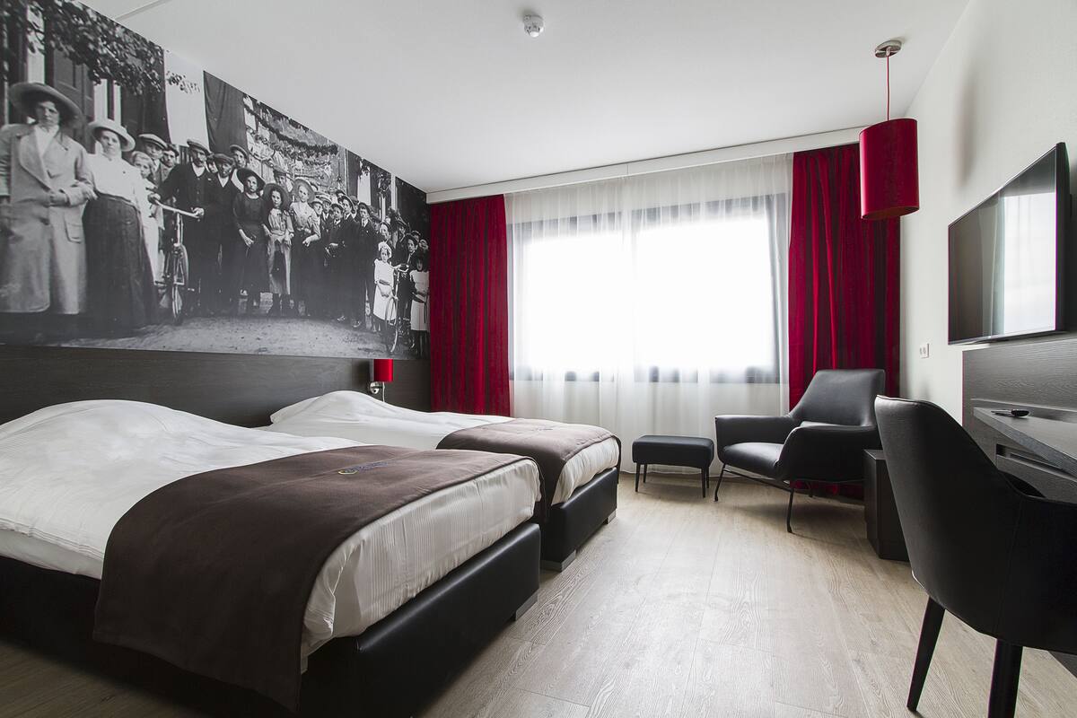 Une chambre d’hôtel avec deux lits, un bureau, une chaise, une télévision et une grande fresque murale.