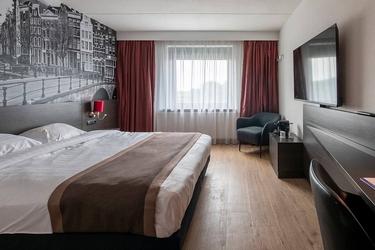 Une chambre d’hôtel moderne, dotée d’un grand lit, d’un bureau, d’une chaise, d’une télévision et d’une fenêtre avec des rideaux.