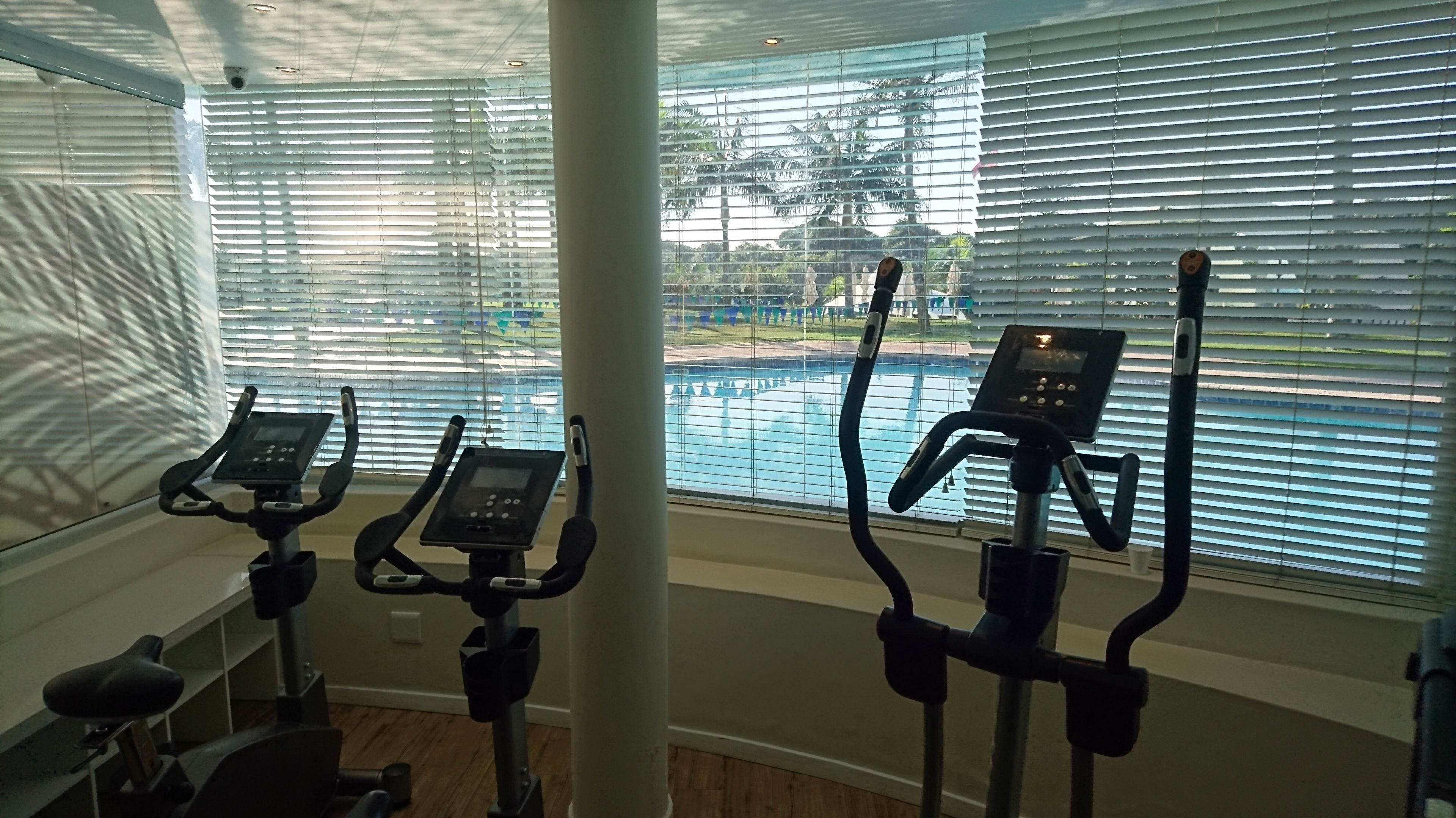 An indoor gym with stationary bikes and a view of a swimming pool through large windows.