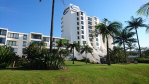 Un hotel moderno con fachada blanca, varios balcones y palmeras en primer plano.