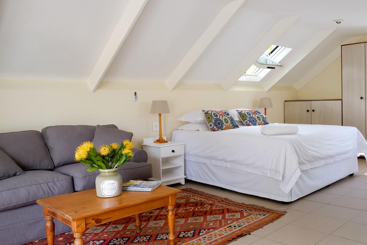 A bedroom with a bed, a sofa, a nightstand, a lamp, a wardrobe, and a window.