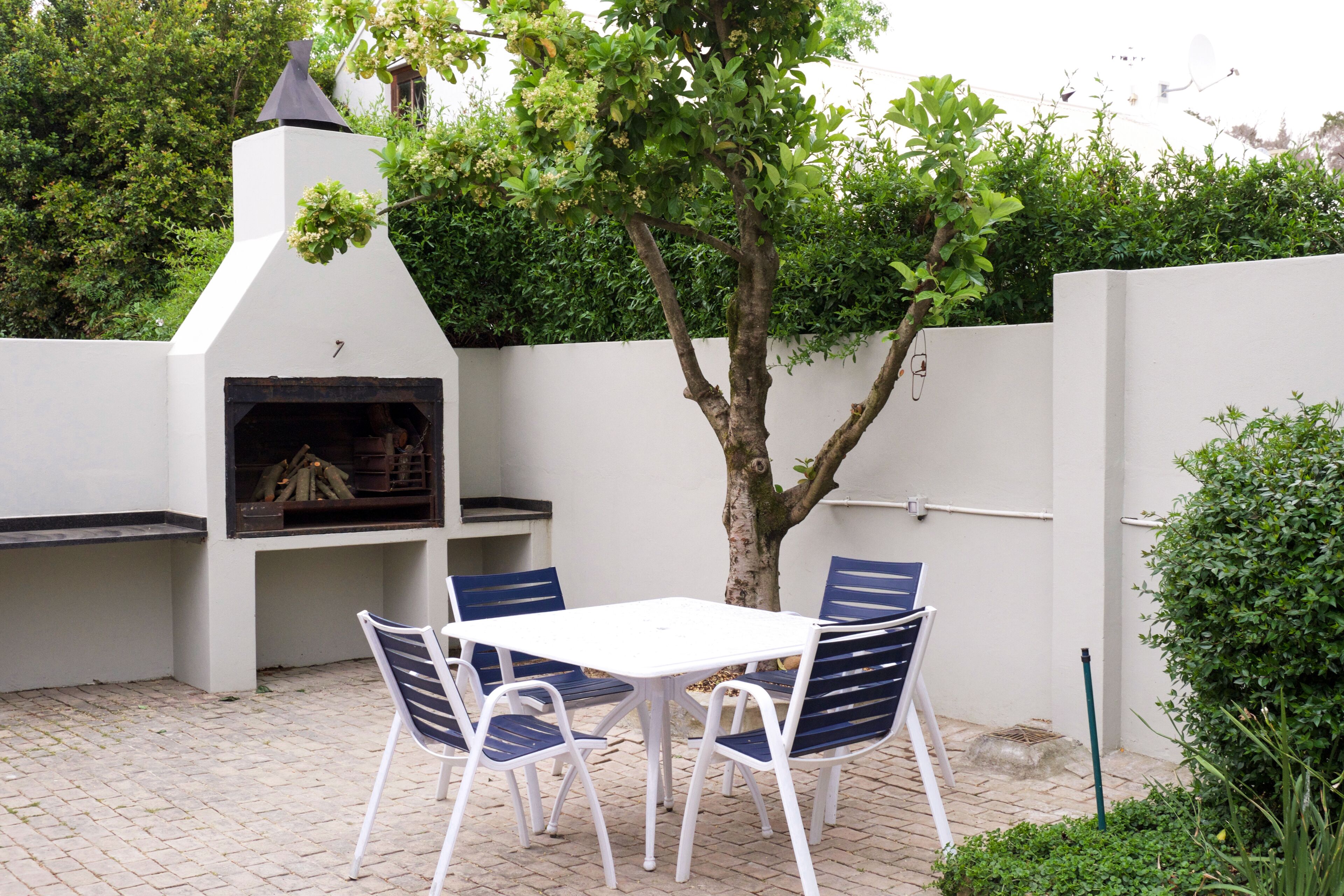 Un patio exterior con una parrilla blanca, una mesa y sillas azules.