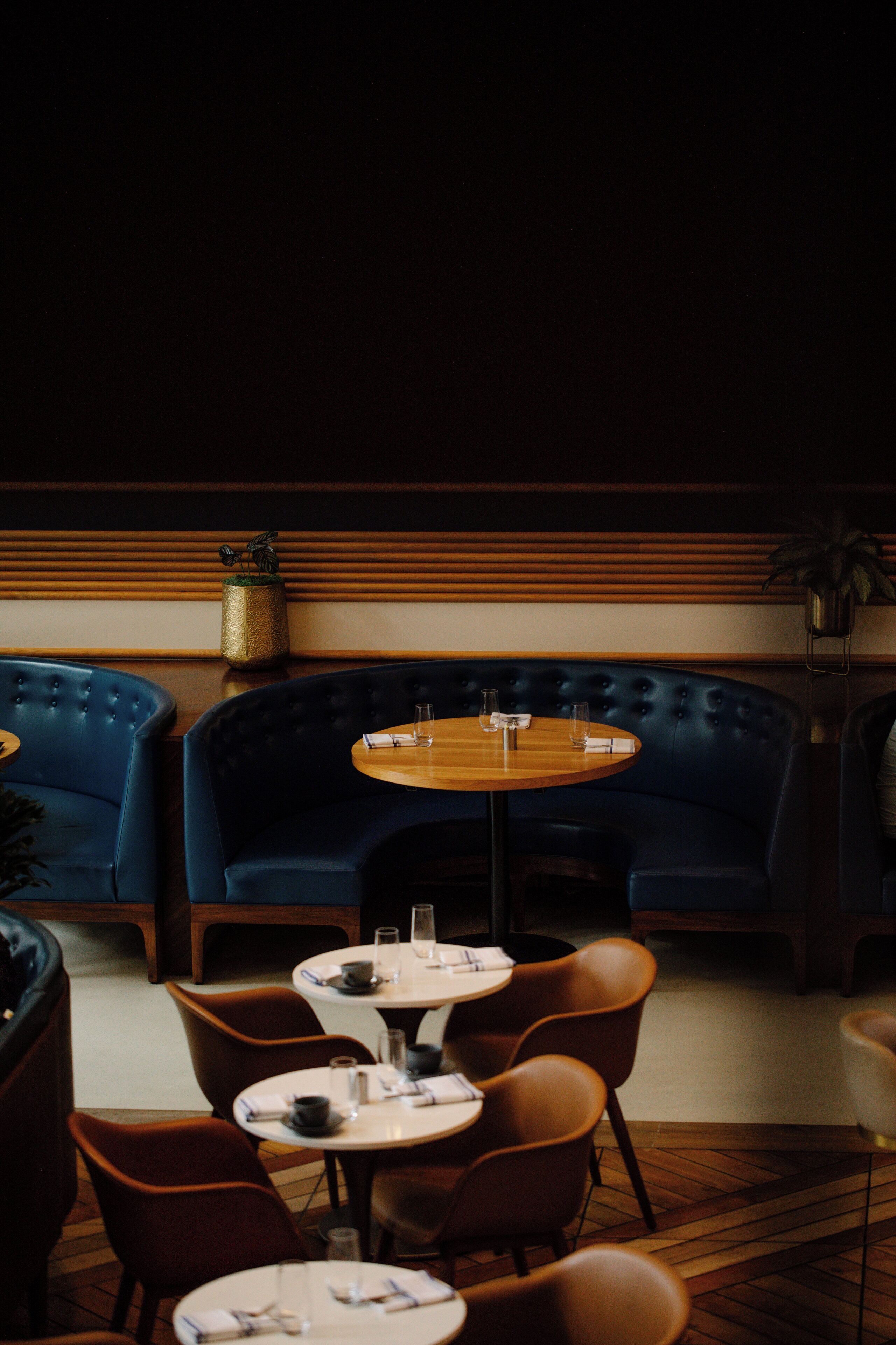 Interior de restaurant amb seients blaus acolxats, taules rodones i cadires marrons.