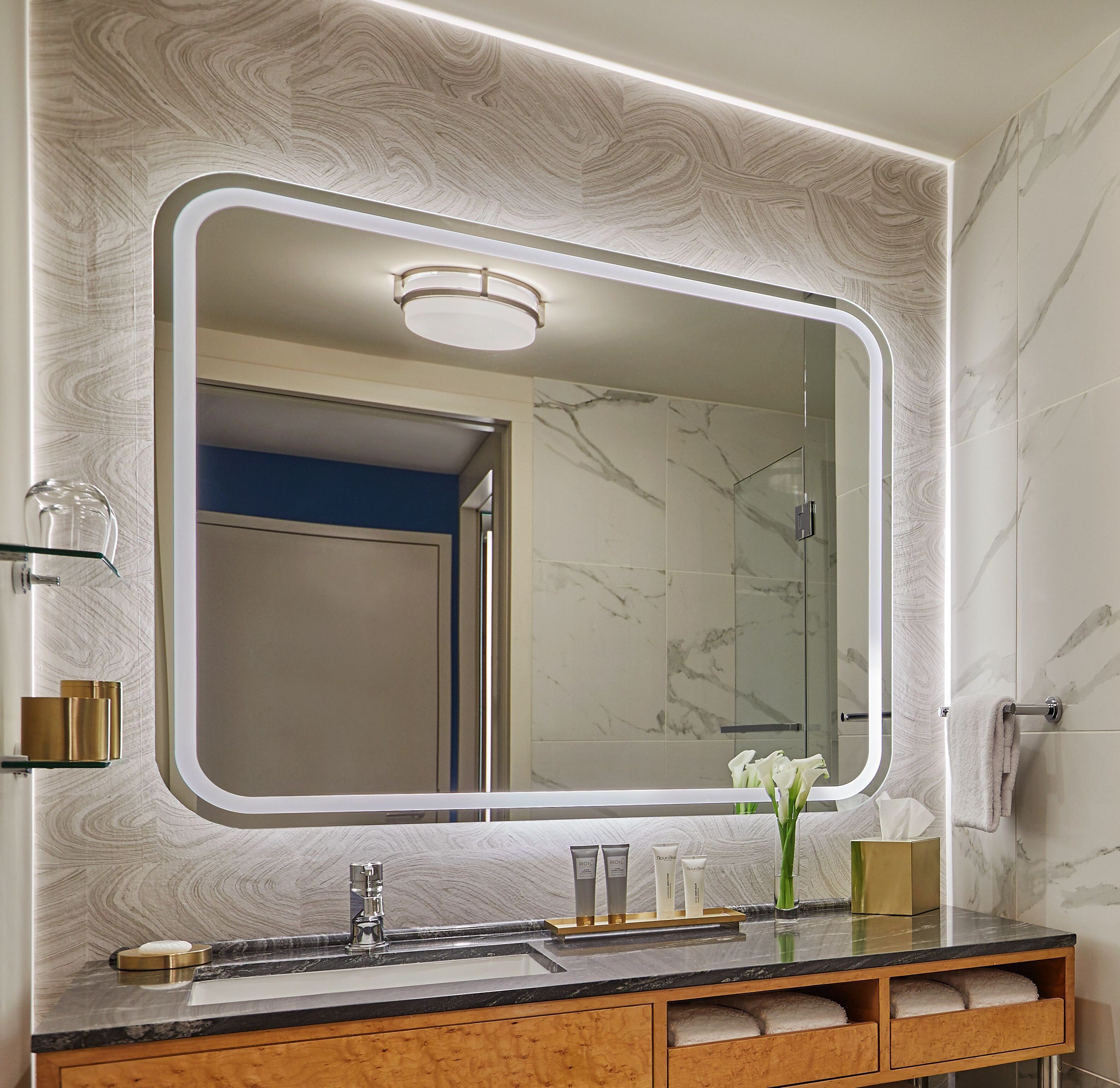 A bathroom with a large mirror, marble walls, a sink with toiletries, and a towel rack.
