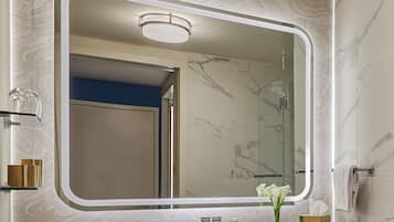 A bathroom with a large mirror, marble walls, a sink with toiletries, and a towel rack.
